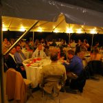 Tent at night with people eating at tables and globe lights